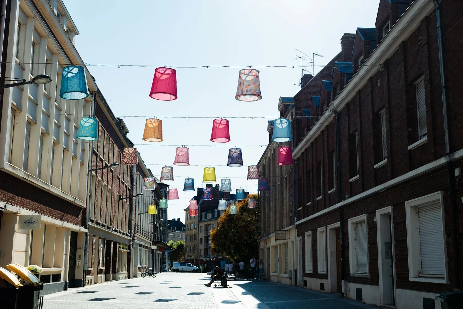 Pantallas de lámparas vibrantes cuelgan sobre una calle de Amiens, Francia, bajo un cielo despejado.